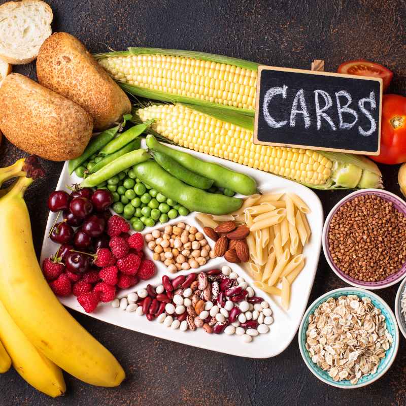 En la fotografía aparece diferentes alimentos ricos en carbohidratos: pan, cereales, frutas, maíz, alubias, guisantes y pasta.